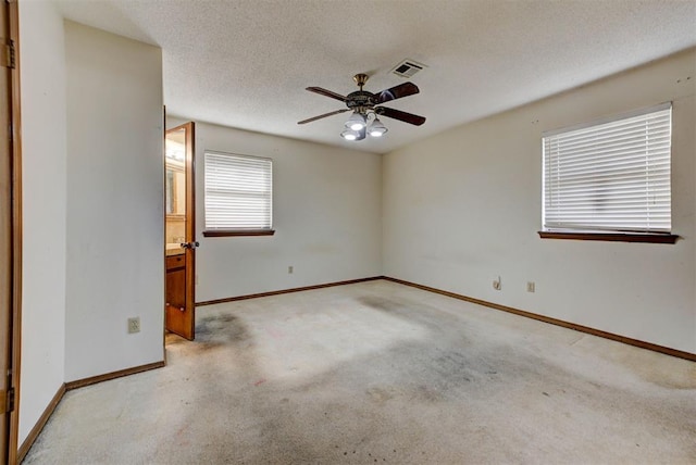 carpeted empty room with a textured ceiling, baseboards, visible vents, and ceiling fan