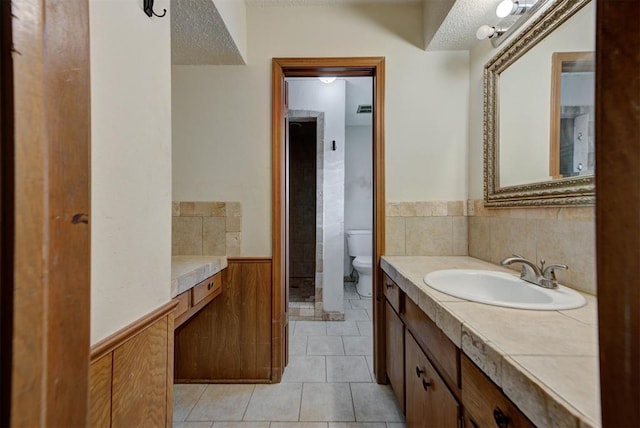 bathroom with tile patterned flooring, wainscoting, a textured ceiling, and toilet