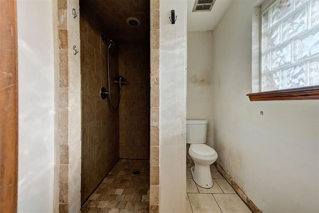 bathroom with tile patterned flooring, toilet, visible vents, and tiled shower