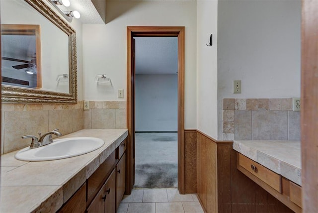 bathroom with tile patterned flooring, vanity, a wainscoted wall, and a textured ceiling