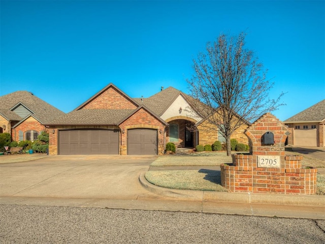 french country style house with brick siding, an attached garage, concrete driveway, and a shingled roof