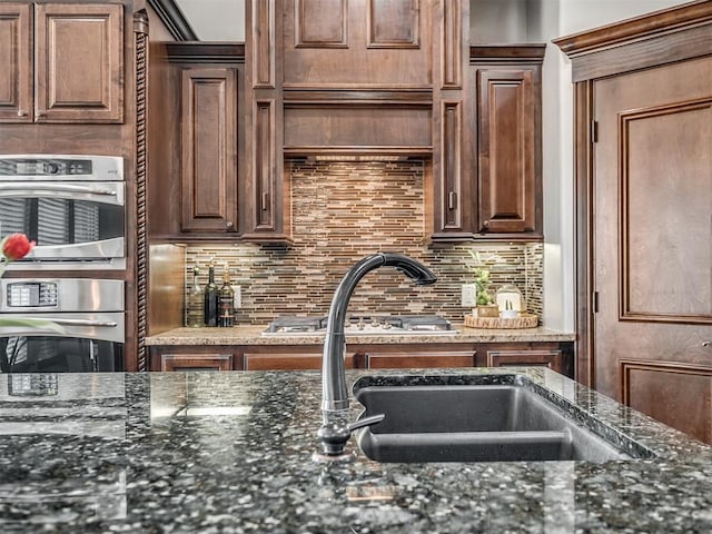 kitchen with tasteful backsplash, dark stone countertops, and a sink