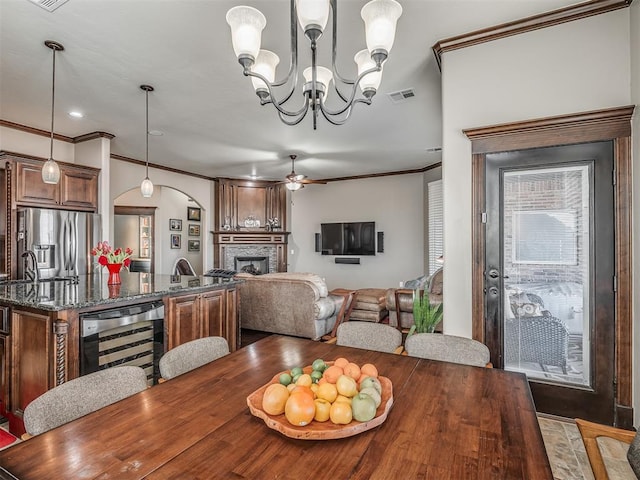 dining space with visible vents, ceiling fan with notable chandelier, wine cooler, arched walkways, and a fireplace