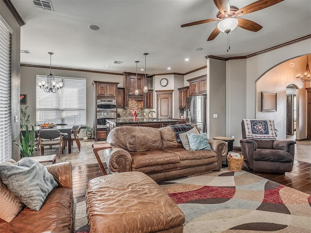 living area featuring light wood-type flooring, visible vents, ornamental molding, ceiling fan with notable chandelier, and arched walkways