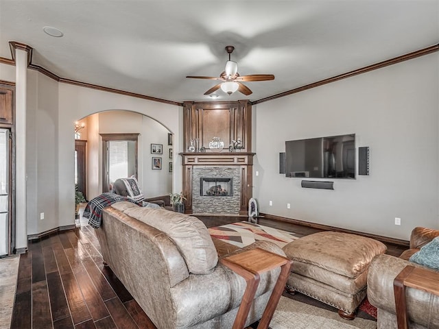 living area featuring baseboards, ceiling fan, dark wood finished floors, a fireplace, and arched walkways