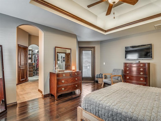 bedroom featuring a walk in closet, a tray ceiling, wood finished floors, a closet, and arched walkways