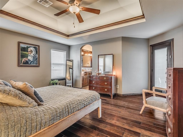 bedroom with a tray ceiling, visible vents, dark wood-style flooring, and ceiling fan