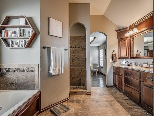 full bathroom with lofted ceiling, stone finish flooring, a tub with jets, baseboards, and vanity