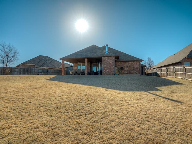 back of house with a yard, brick siding, a fenced backyard, and a shingled roof