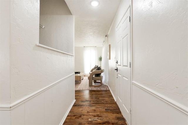 hall featuring a textured ceiling, dark wood-style floors, wainscoting, a decorative wall, and a textured wall