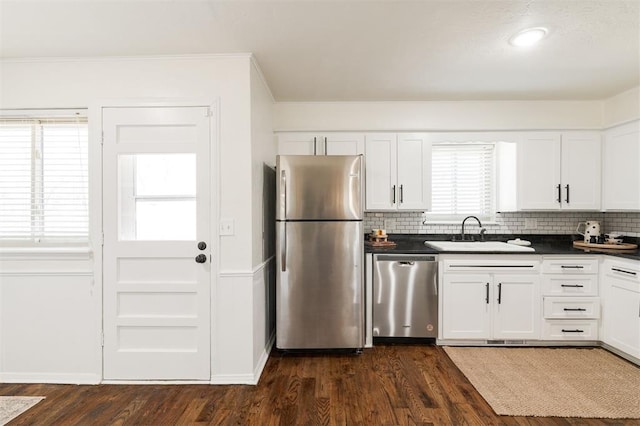 kitchen featuring dark countertops, backsplash, dark wood-type flooring, stainless steel appliances, and a sink