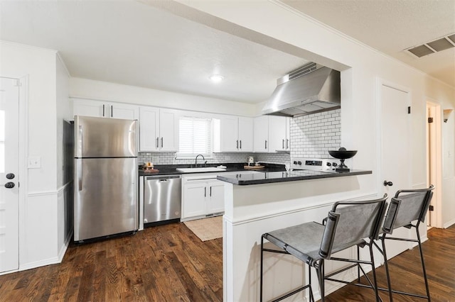 kitchen with visible vents, a sink, appliances with stainless steel finishes, dark countertops, and wall chimney range hood