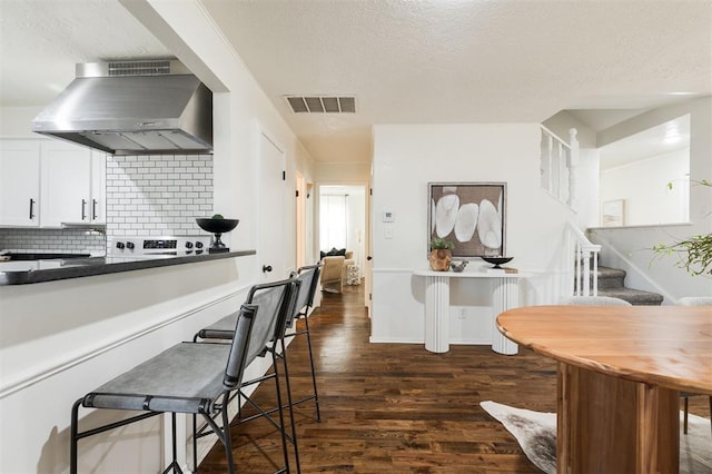 kitchen with visible vents, dark wood finished floors, decorative backsplash, range hood, and white cabinetry