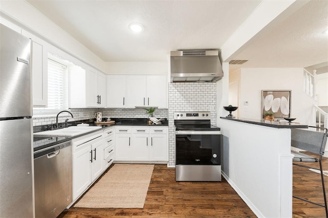 kitchen with visible vents, dark wood-style flooring, a sink, stainless steel appliances, and wall chimney range hood