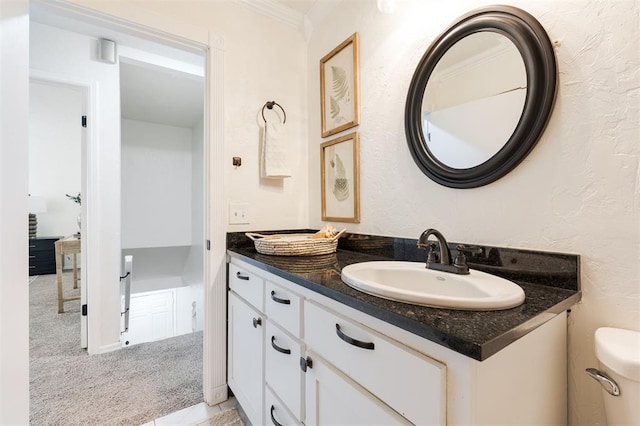 bathroom with a textured wall, toilet, vanity, and crown molding