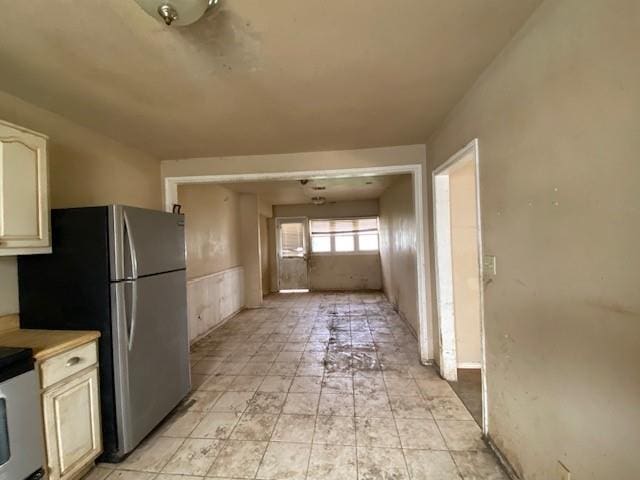 kitchen featuring stove, cream cabinetry, light countertops, and freestanding refrigerator