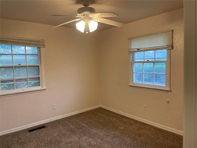 unfurnished room with plenty of natural light, a ceiling fan, visible vents, and dark carpet