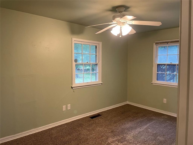 unfurnished room featuring visible vents, a healthy amount of sunlight, a ceiling fan, and dark colored carpet