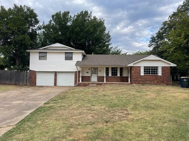 tri-level home with brick siding, covered porch, a garage, and fence