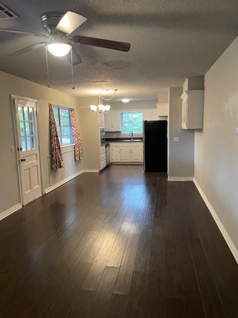 unfurnished living room featuring visible vents, ceiling fan with notable chandelier, a sink, plenty of natural light, and dark wood-style flooring