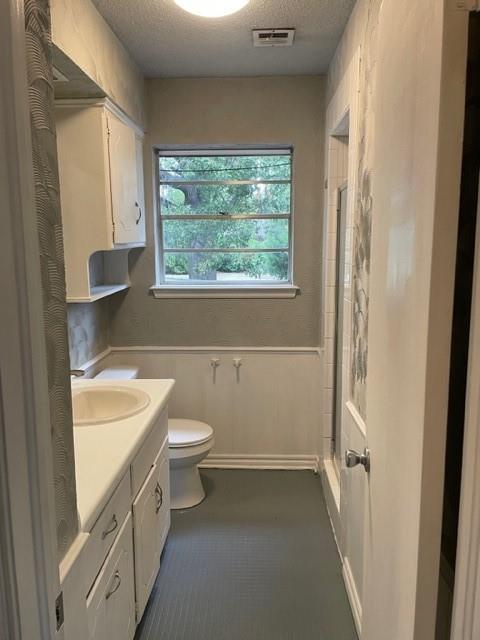 full bathroom featuring visible vents, toilet, wainscoting, a textured ceiling, and a shower