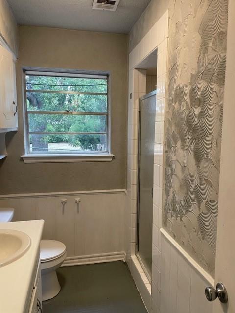 bathroom featuring vanity, toilet, a tile shower, and wainscoting