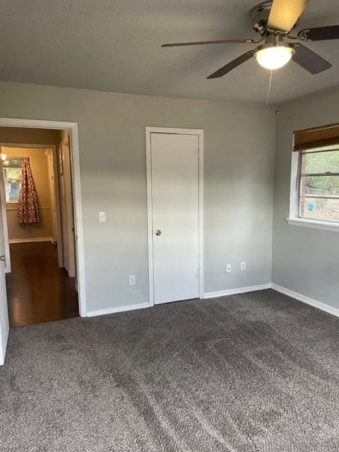 unfurnished bedroom featuring a ceiling fan, baseboards, dark colored carpet, and a textured ceiling