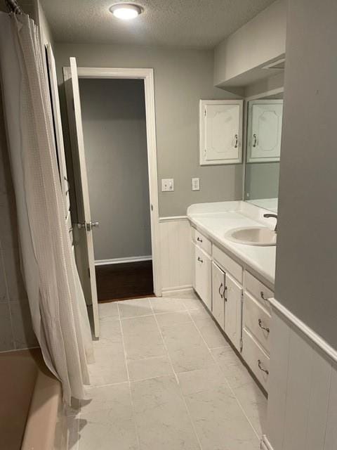 bathroom with shower / tub combo with curtain, wainscoting, a textured ceiling, and vanity