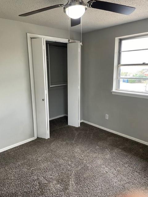 unfurnished bedroom with a ceiling fan, baseboards, a closet, a textured ceiling, and dark colored carpet