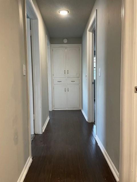 corridor with dark wood-style floors, baseboards, and a textured ceiling