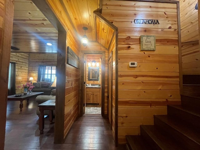 hall with wooden walls, dark wood finished floors, stairs, wooden ceiling, and a sink