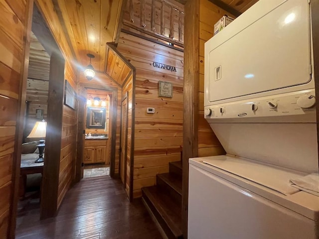 interior space featuring stacked washing maching and dryer, dark wood finished floors, laundry area, a sink, and wood walls