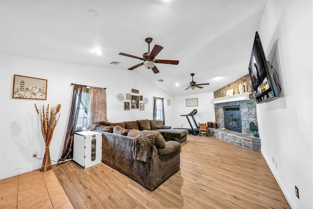 living room featuring wood finished floors, a ceiling fan, visible vents, lofted ceiling, and a stone fireplace