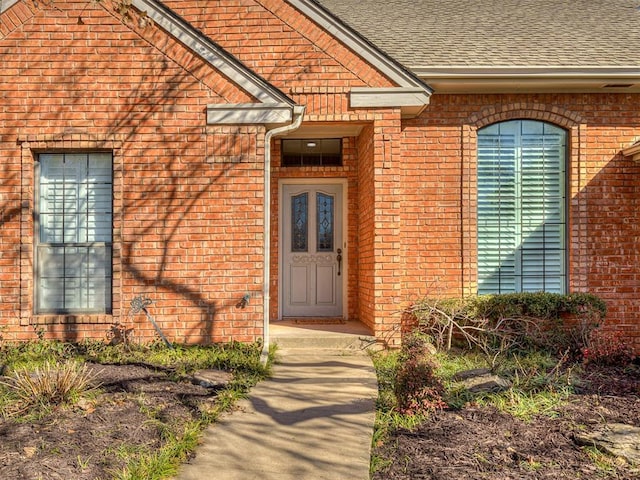 doorway to property with brick siding and roof with shingles