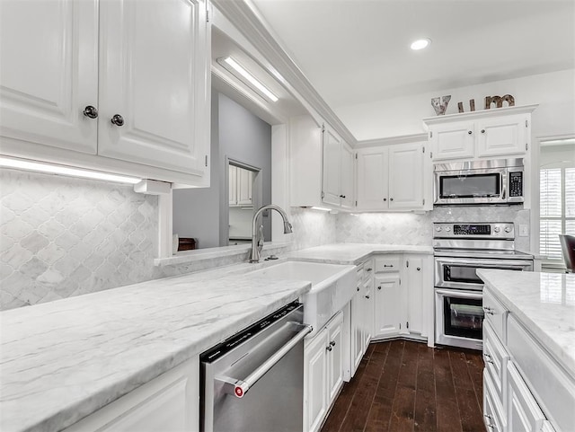 kitchen with a sink, light stone counters, appliances with stainless steel finishes, white cabinetry, and dark wood-style flooring