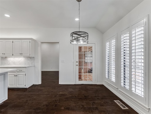 unfurnished dining area featuring visible vents, dark wood-type flooring, a notable chandelier, and plenty of natural light