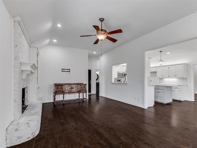 living room featuring ceiling fan, dark wood finished floors, lofted ceiling, a fireplace, and stacked washing maching and dryer