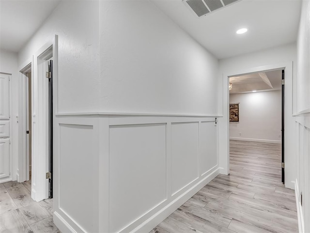 hallway with a decorative wall, light wood-style floors, visible vents, and wainscoting