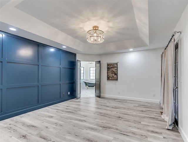 empty room featuring baseboards, light wood-style floors, a raised ceiling, a decorative wall, and a notable chandelier