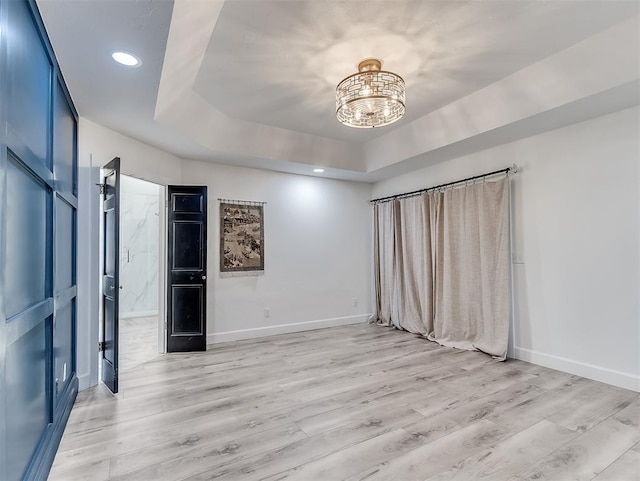 spare room featuring light wood finished floors, baseboards, a chandelier, a tray ceiling, and recessed lighting