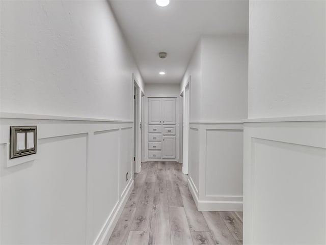 hall with recessed lighting, a decorative wall, light wood-style flooring, and a wainscoted wall