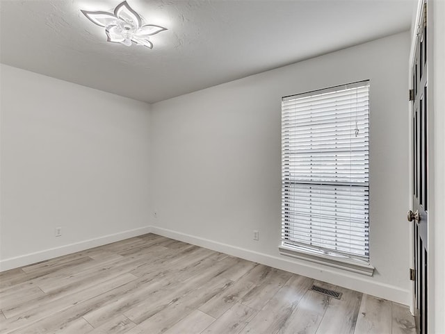 spare room featuring light wood finished floors, visible vents, and baseboards