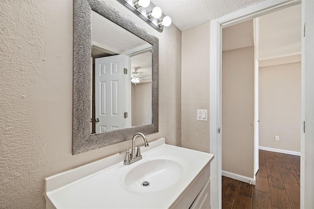 bathroom featuring baseboards, wood finished floors, vanity, a textured wall, and a textured ceiling