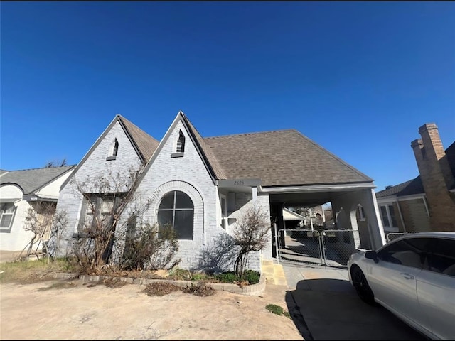 view of front of house with a gate, roof with shingles, concrete driveway, a carport, and brick siding