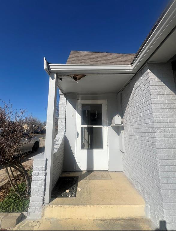 view of exterior entry featuring a shingled roof