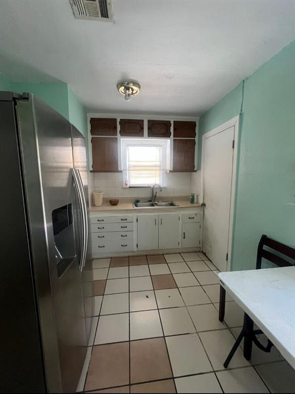 kitchen with visible vents, open shelves, a sink, light countertops, and stainless steel refrigerator with ice dispenser