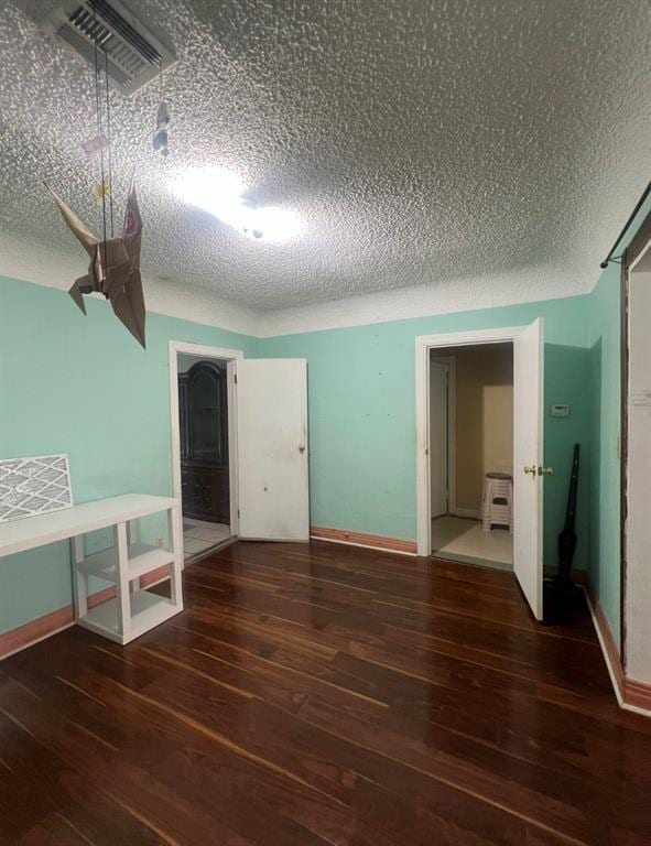 empty room with baseboards, wood finished floors, visible vents, and a textured ceiling