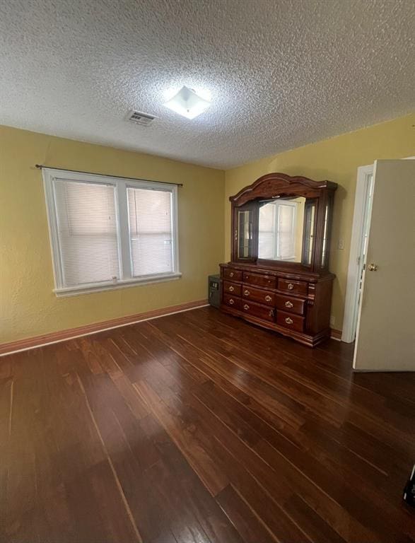 unfurnished bedroom with visible vents, baseboards, a textured ceiling, and wood finished floors