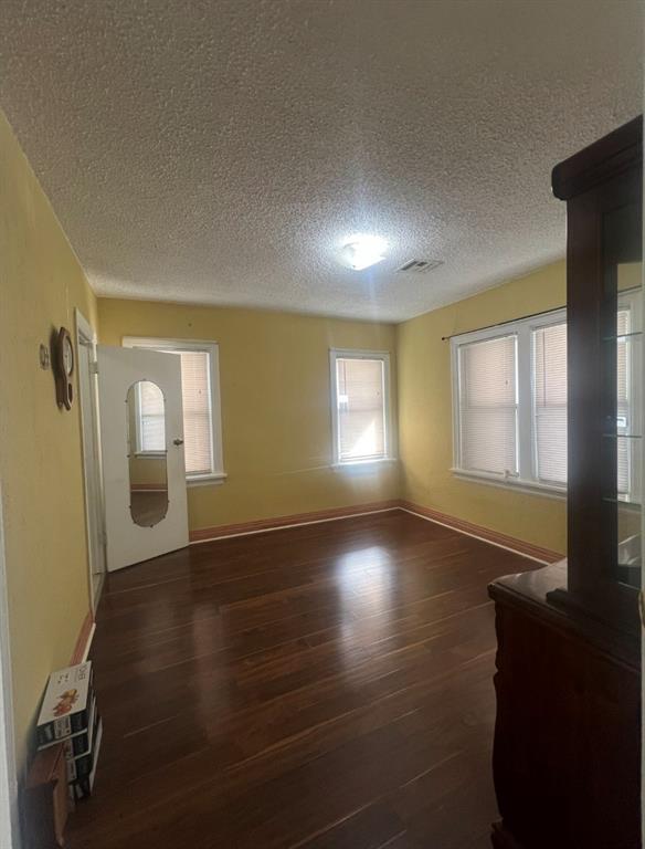 unfurnished living room with visible vents, a textured ceiling, baseboards, and wood finished floors