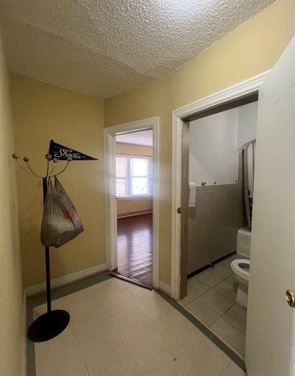 hall featuring tile patterned floors, a textured ceiling, and baseboards